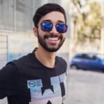 Portrait of a smiling man wearing sunglasses outdoors, showcasing modern fashion and style.